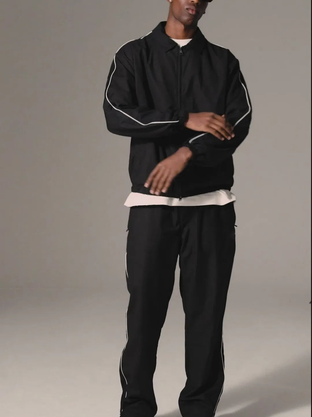 Person wearing a black tracksuit with white piping on a plain background