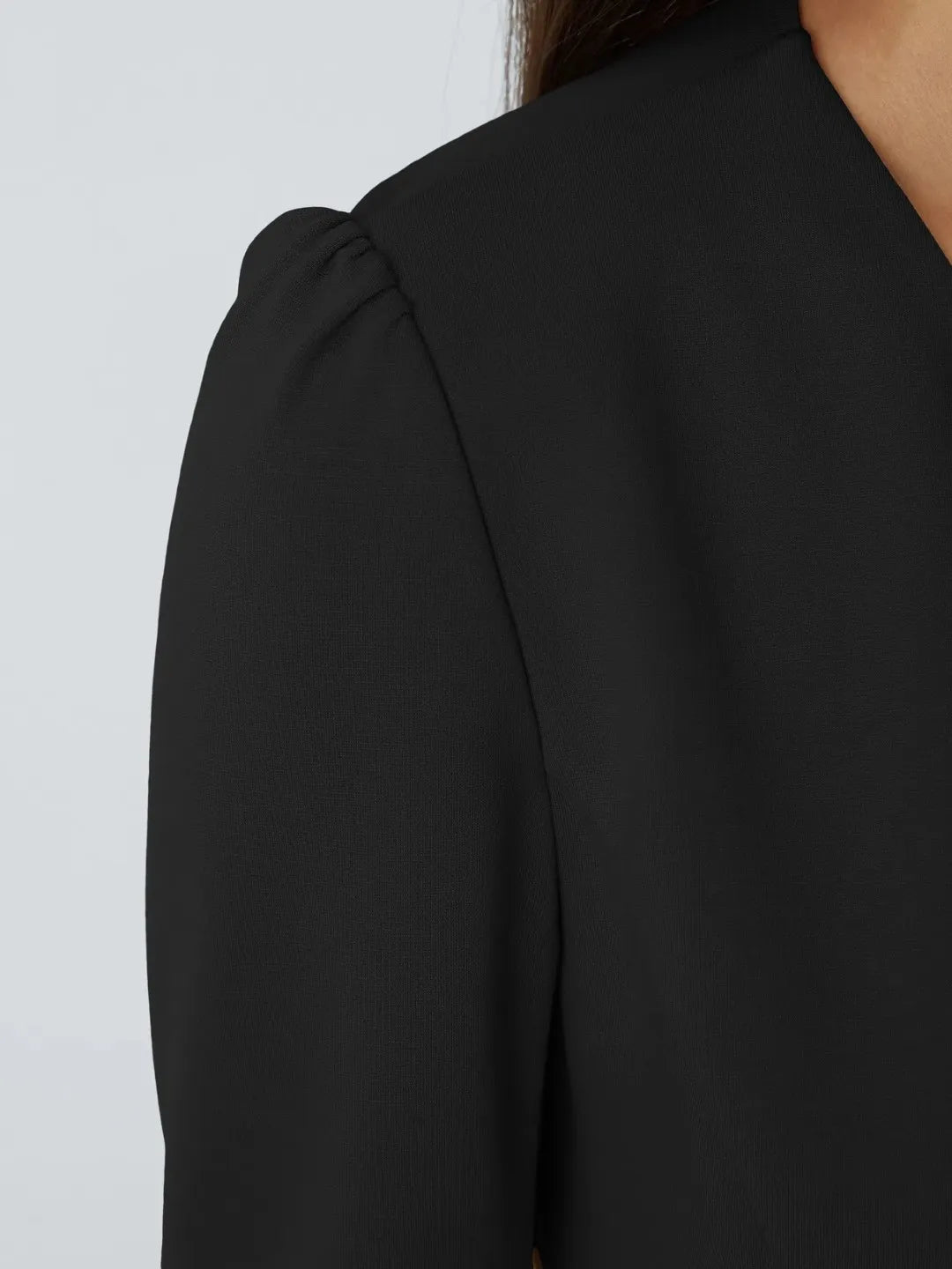 Woman wearing a black buisness jacket with gold buttons on a light gray background