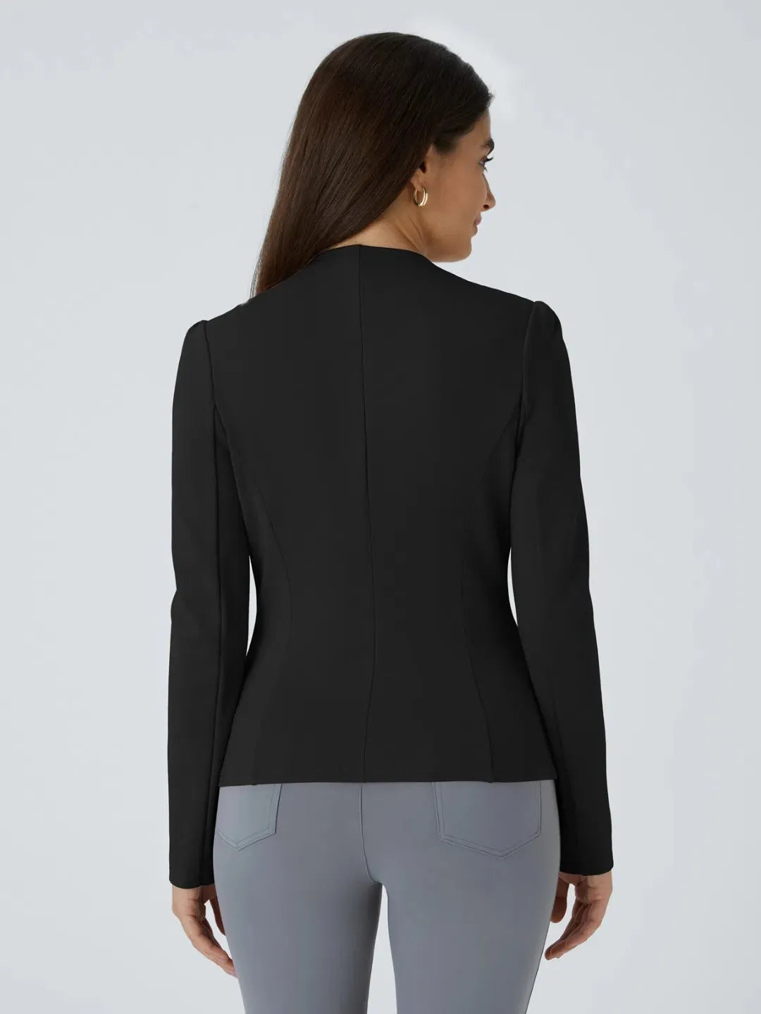 Woman wearing a black buisness jacket with gold buttons on a light gray background