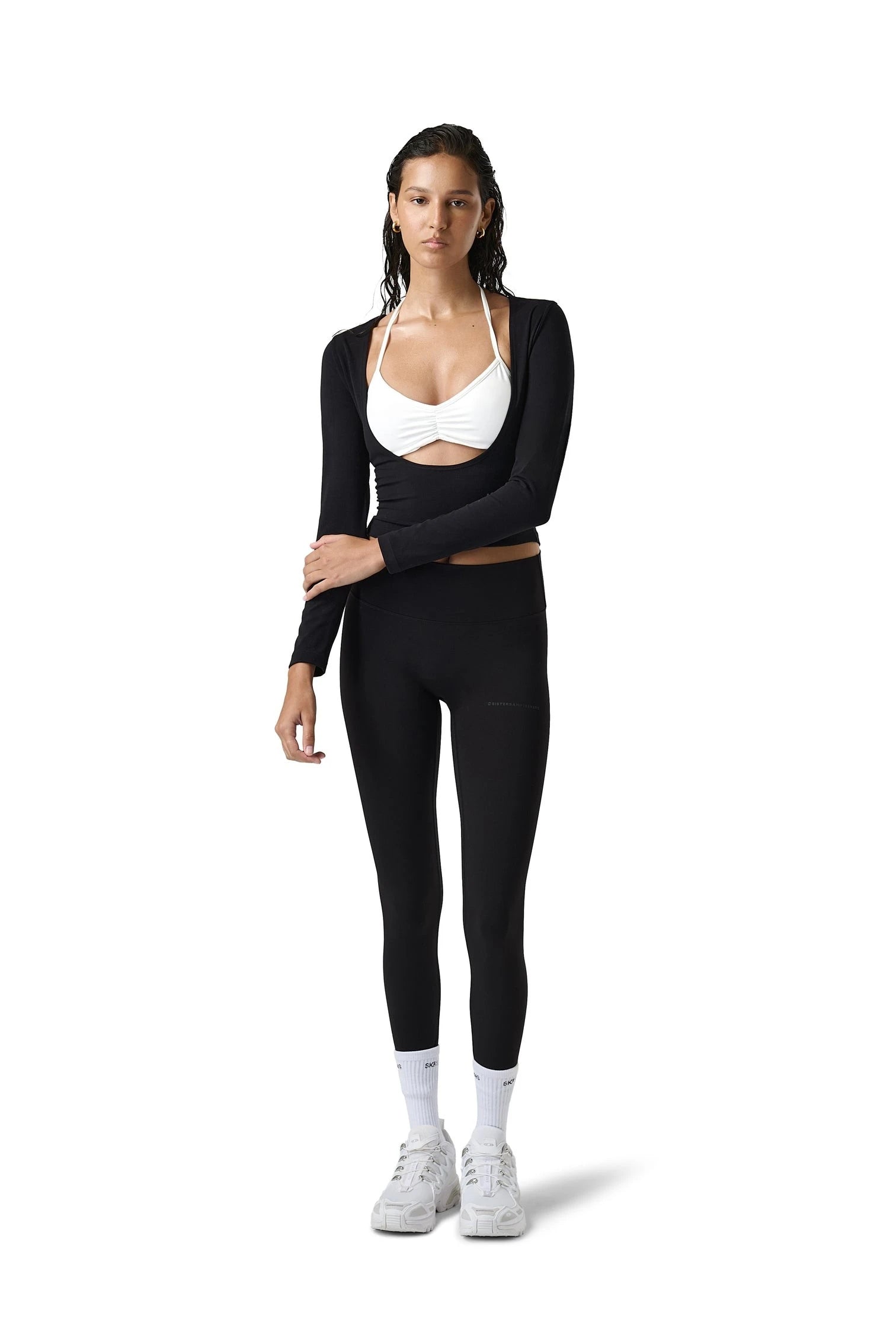 Woman wearing a black long-sleeve top and leggings with a white sports bra on a white background