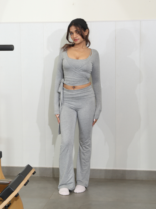 Woman wearing a grey pilates outfit standing in a room with a whiteboard.