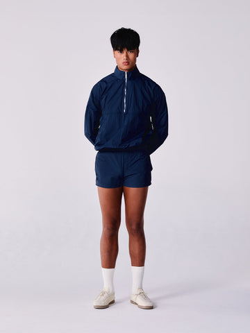 Person wearing a navy blue tracksuit with white socks and shoes on a light grey background