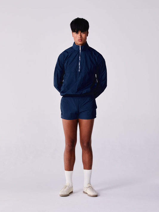 Person wearing a navy blue tracksuit with white socks and shoes on a light grey background