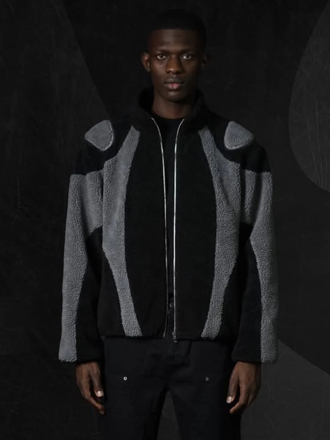 Person wearing a black and grey patterned jacket against a dark background
