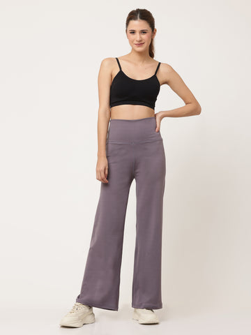 A woman standing and posing in lavender high-waisted full-length yoga pants with a solid black sports top.