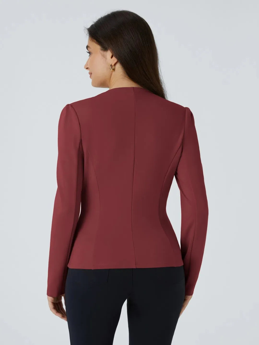 Woman wearing a maroon buisness jacket with gold buttons on a light gray background