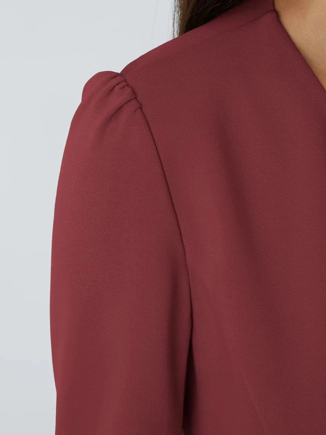 Woman wearing a maroon buisness jacket with gold buttons on a light gray background