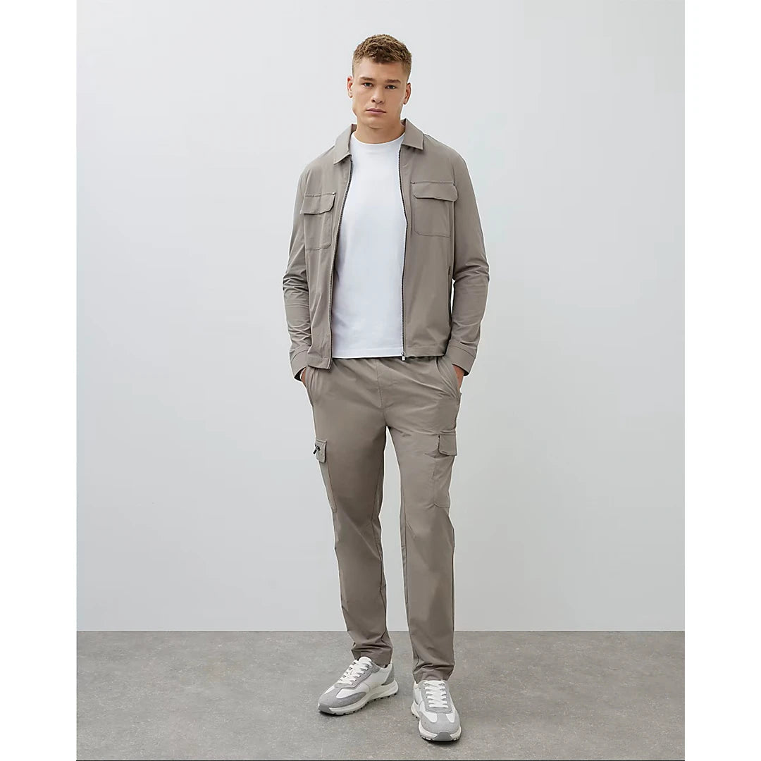 Man wearing a beige jacket and pants with white sneakers on a plain background