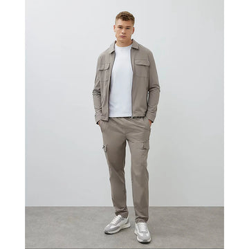 Man wearing a beige jacket and pants with white sneakers on a plain background