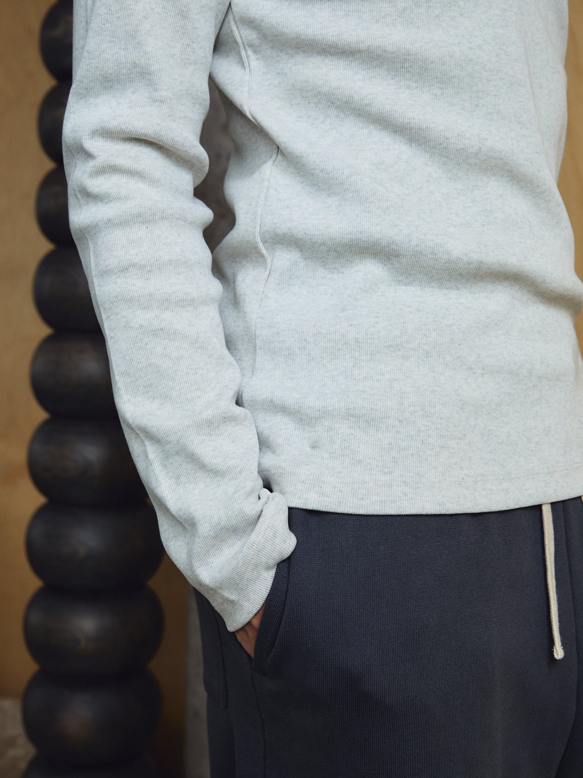 Person wearing a light grey sweatshirt and dark pants with a beige background