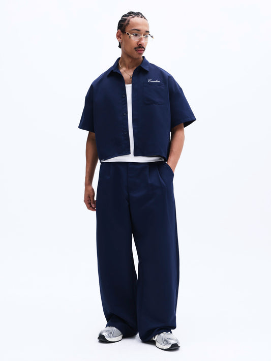 Person wearing a navy blue outfit with a white shirt underneath on a white background