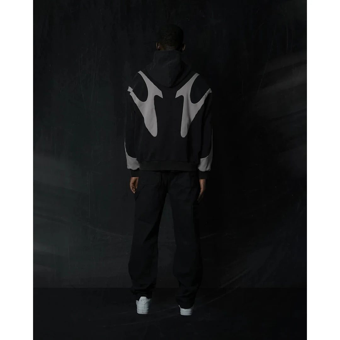 Person wearing a black hoodie with a large white symbol on the back against a dark background