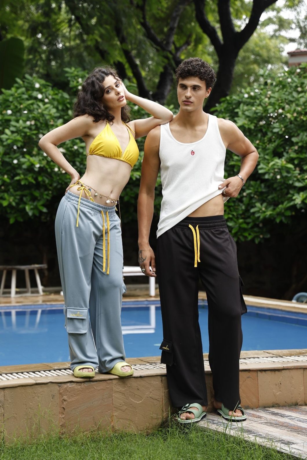 Two people standing by a poolside with greenery in the background
