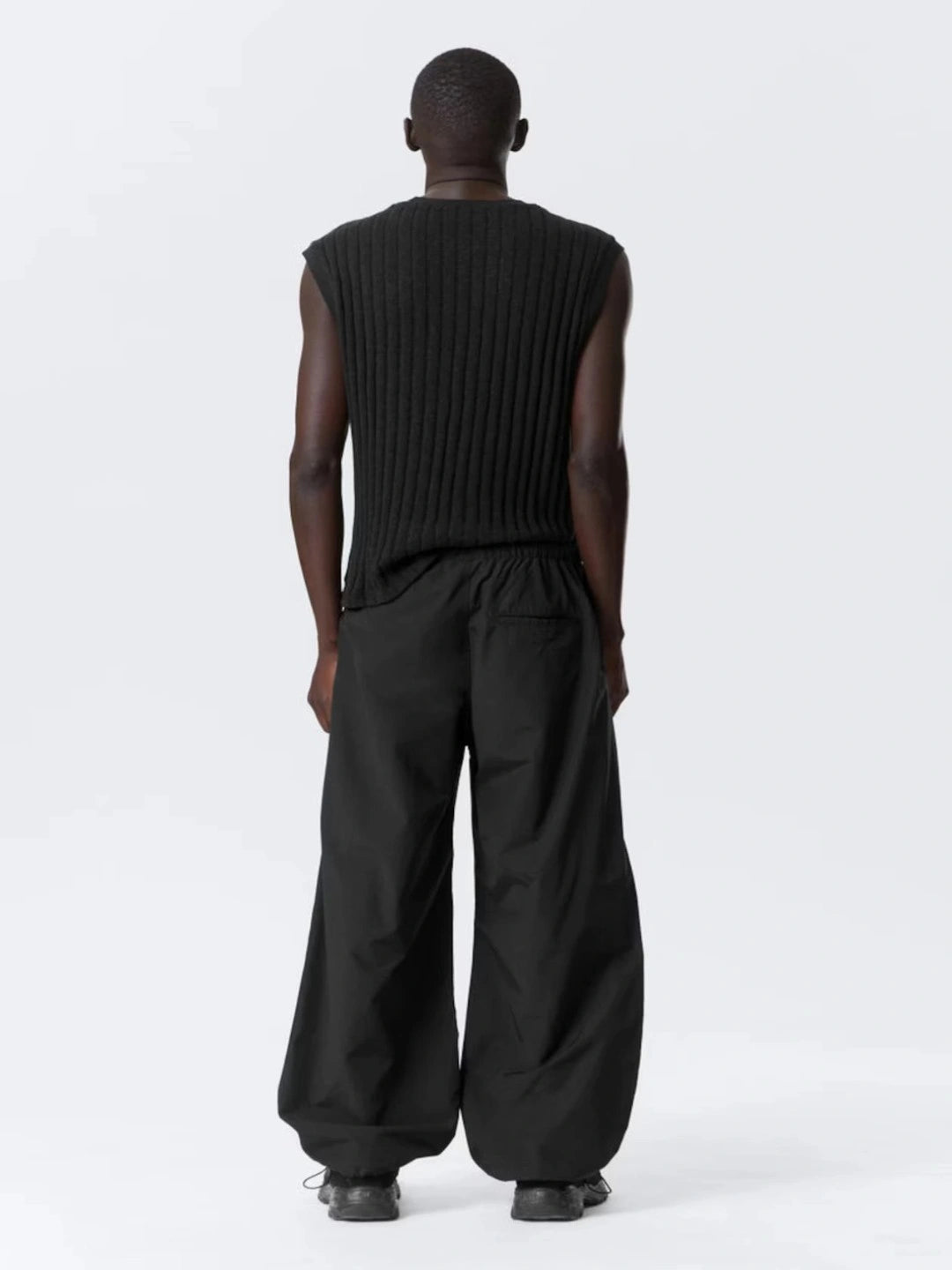Person wearing a black sleeveless top and wide-leg pants on a white background