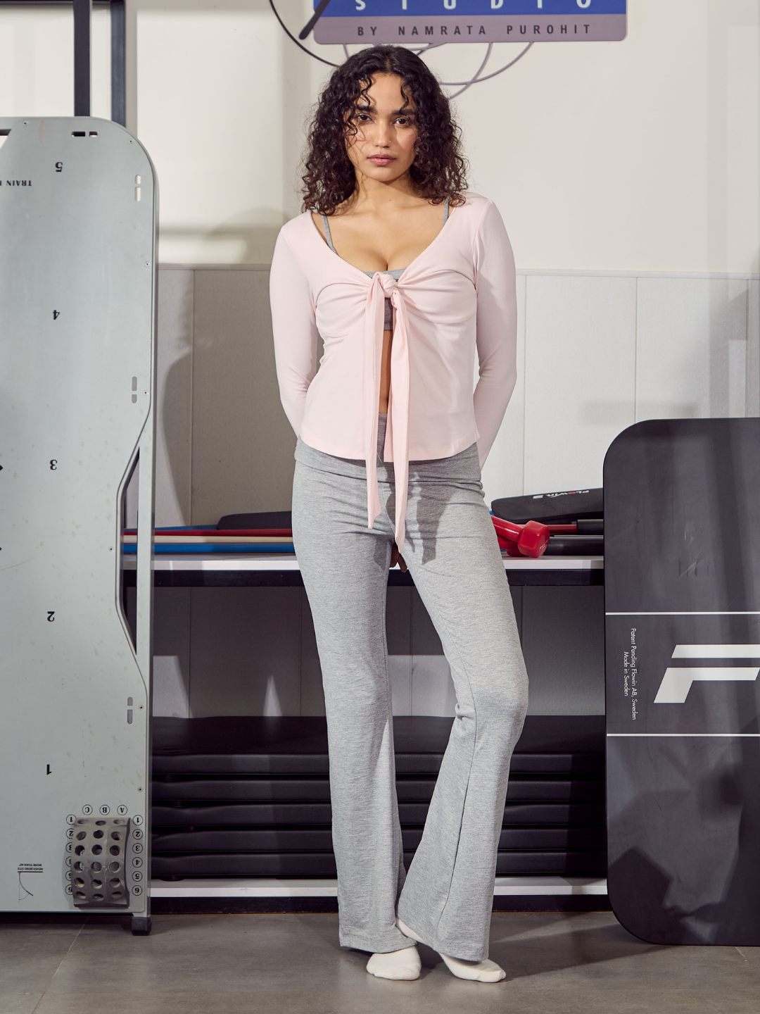 Woman in a pink top and grey pants standing in front of gym equipment