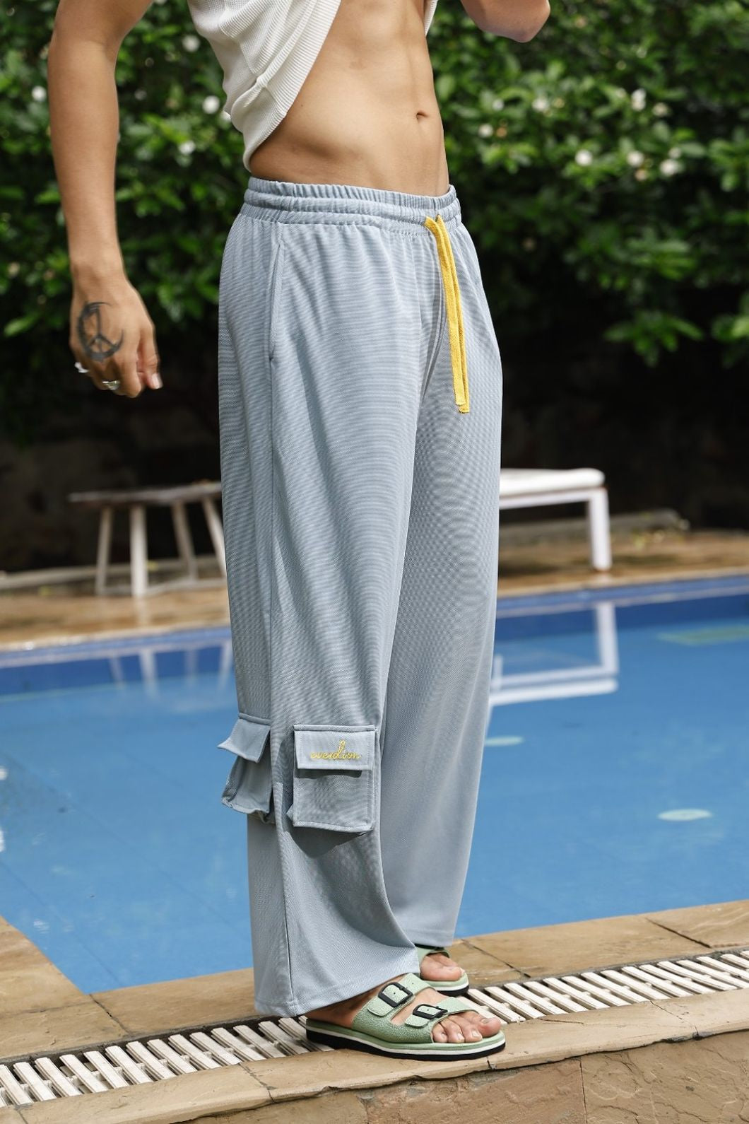 Person wearing light gray mesh pants with a yellow zipper by a poolside.