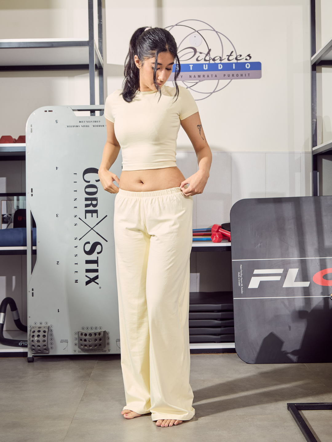 Woman in a beige outfit standing in a fitness studio with equipment in the background