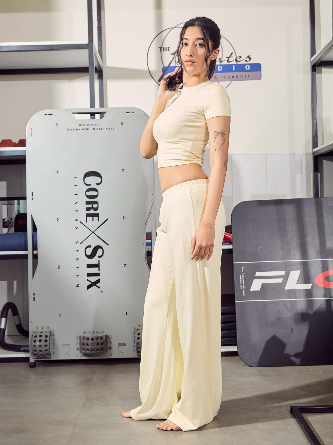 Woman in a white outfit standing in a fitness studio with exercise equipment in the background