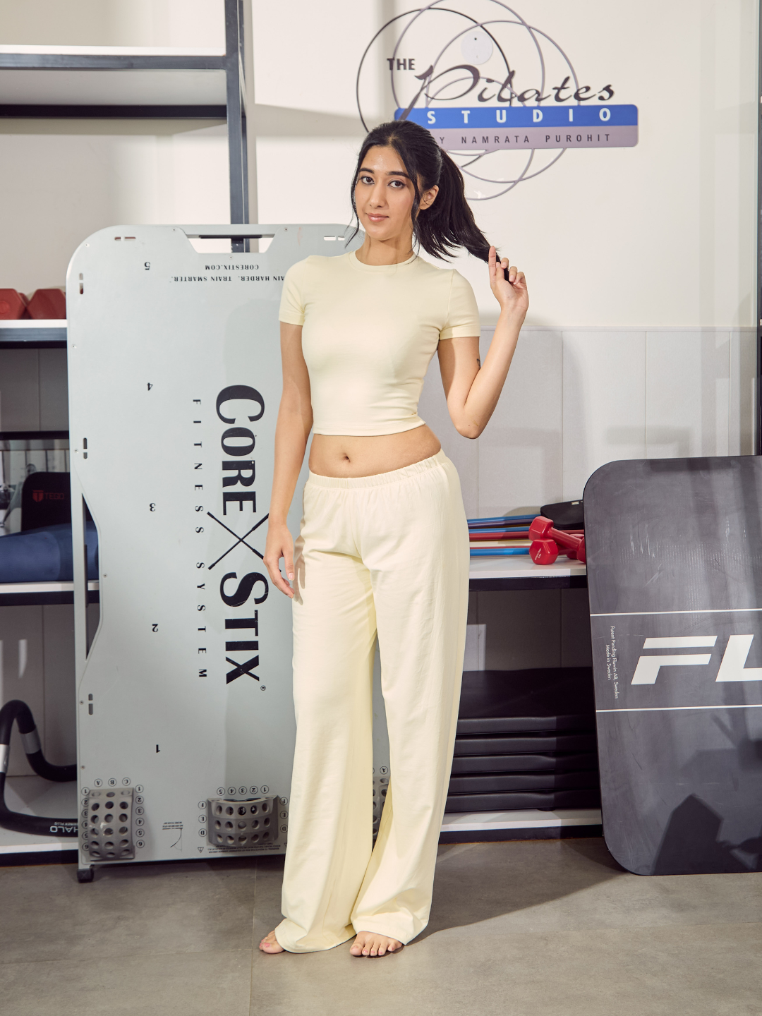 Woman in a Pilates studio wearing a white outfit with fitness equipment in the background.
