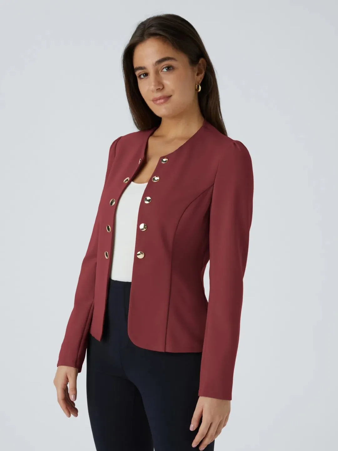 Woman wearing a maroon buisness jacket with gold buttons on a light gray background