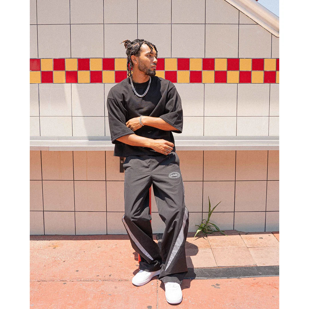 Person wearing a dark gray outfit with white sneakers standing against a tiled wall.