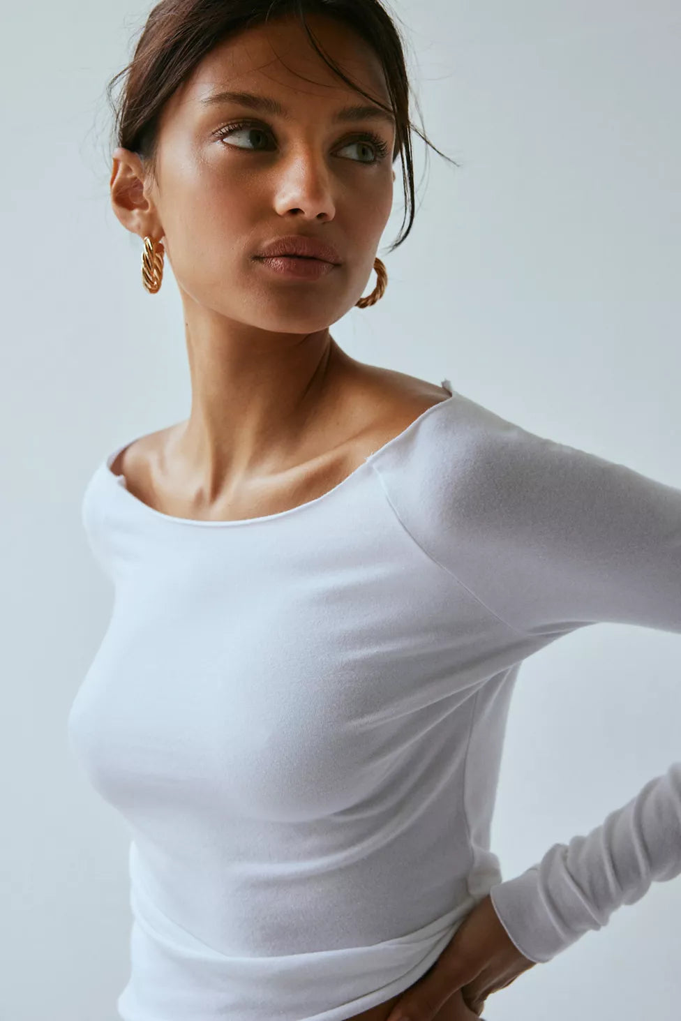 Woman wearing a white long-sleeve top against a plain background