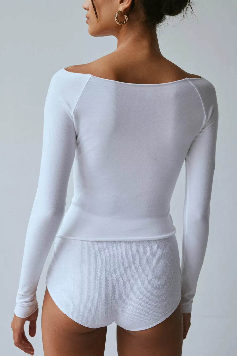 White long-sleeve bodysuit worn by a person on a plain background