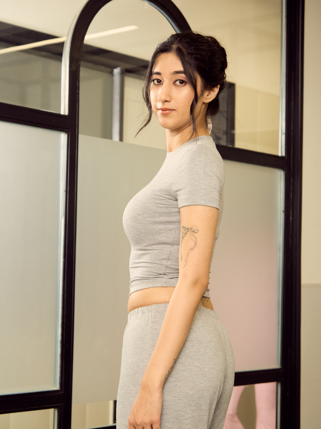 Woman in grey athletic wear standing in front of a mirror.