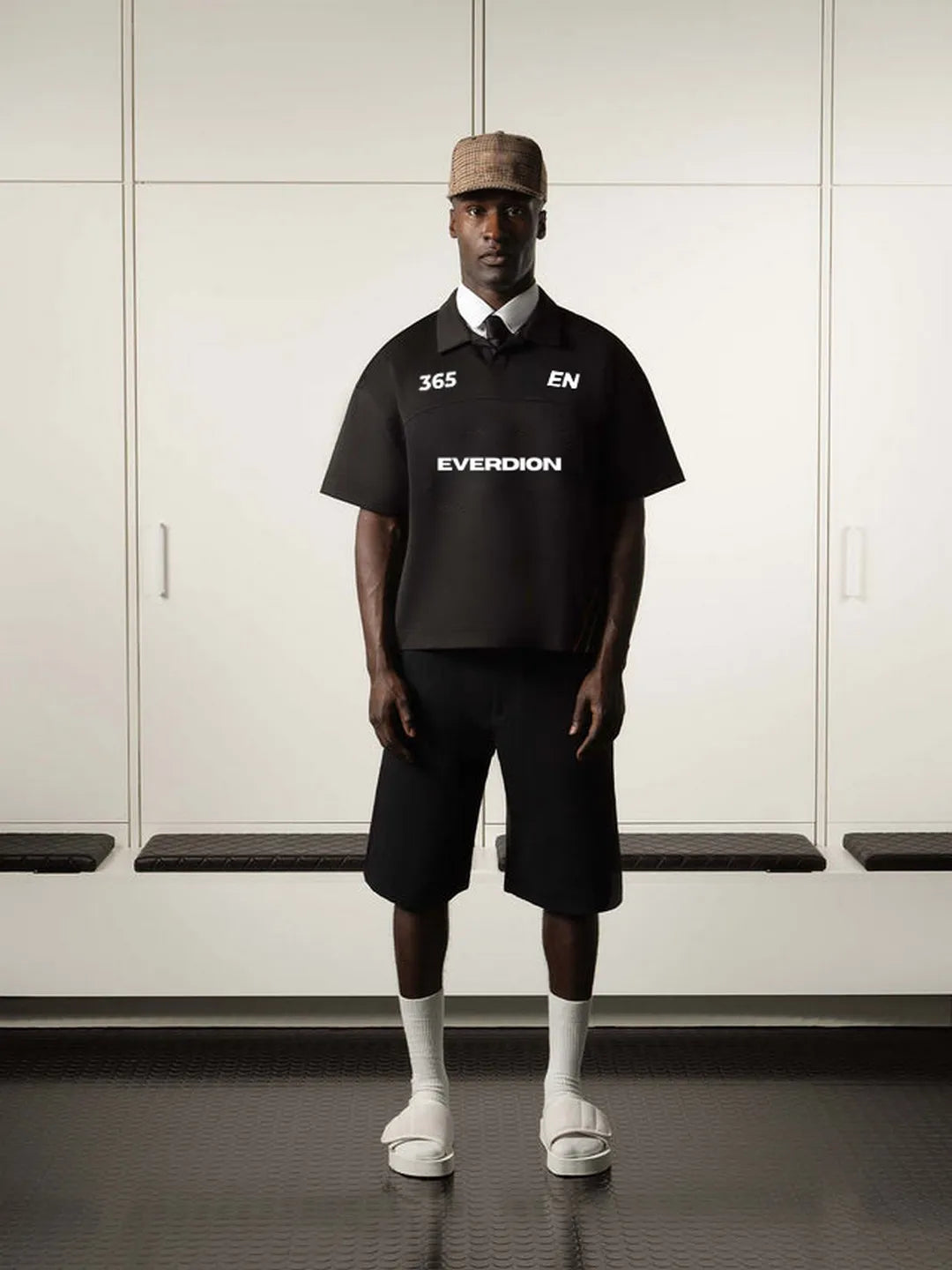 Person wearing a black polo shirt with branding in a locker room setting
