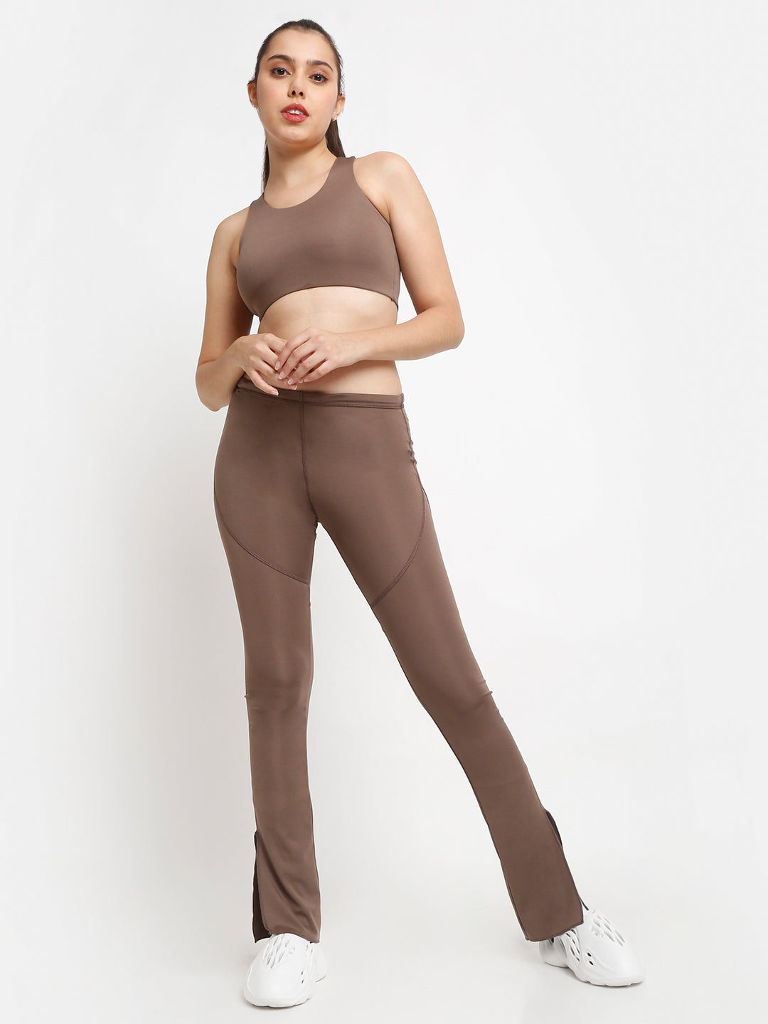 A woman wearing a brown racerback sports bra and matching leggings, standing against a white background.