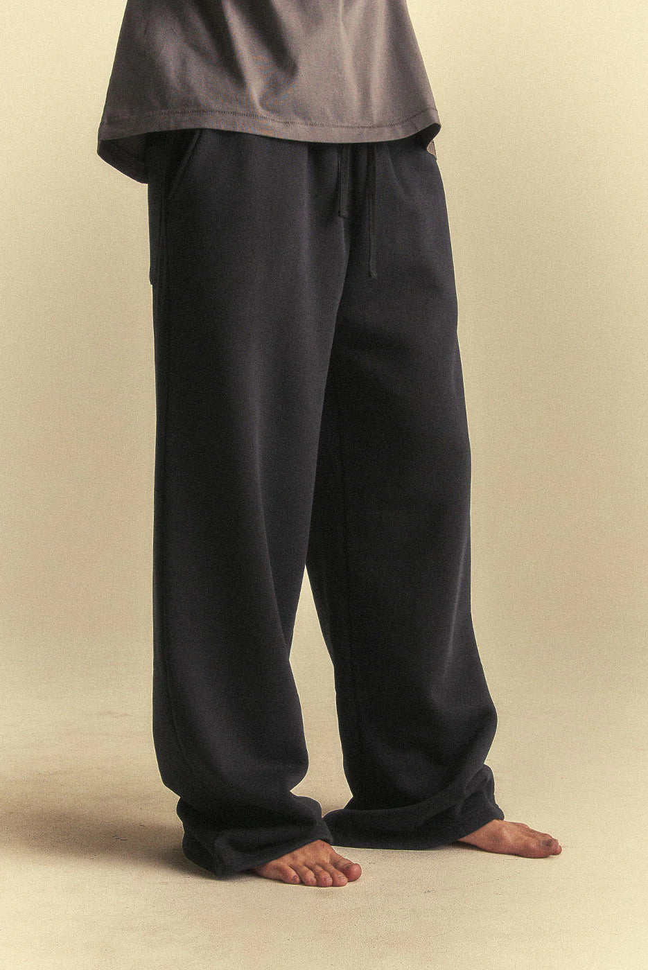 Person wearing black pants and a grey top on a beige background