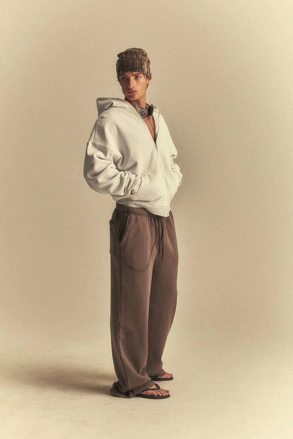 Person wearing a white hoodie and brown pants on a beige background