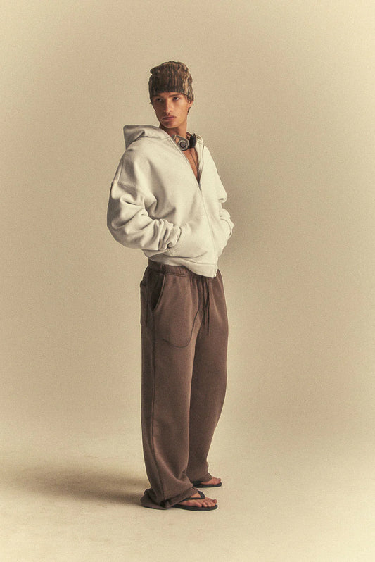 Person wearing a white hoodie and brown pants on a beige background