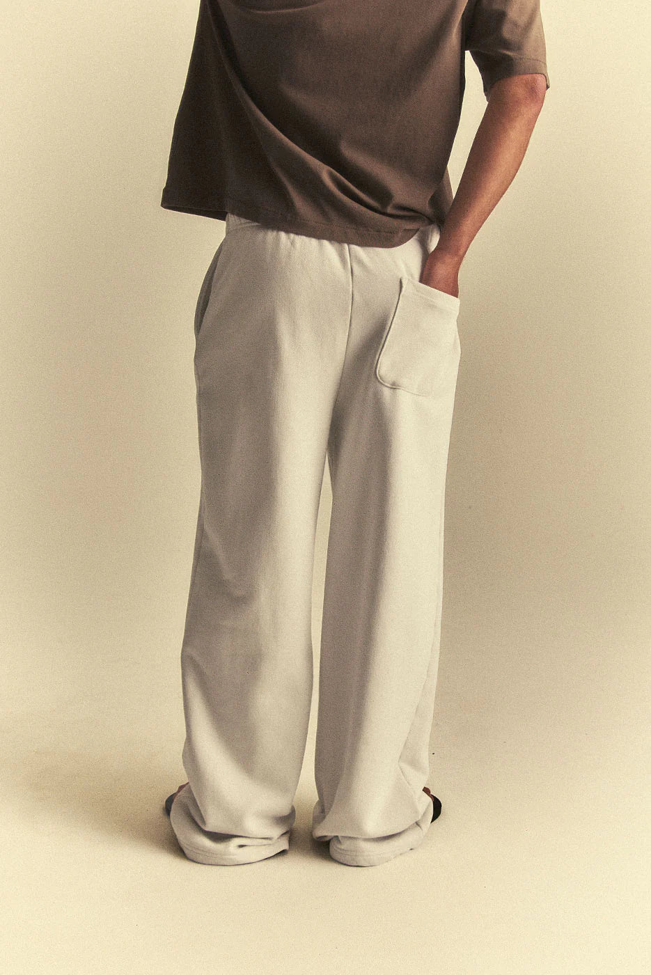 Person wearing light grey pants and a brown shirt on a beige background