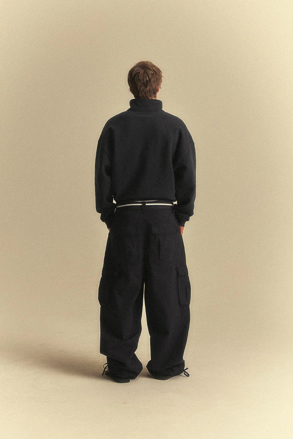 Person wearing a black outfit against a beige background