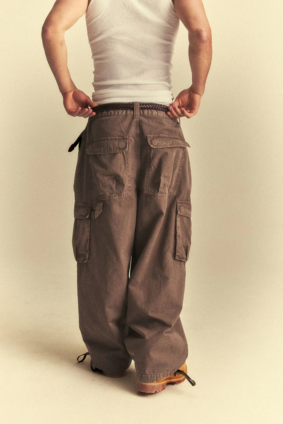 Person wearing brown cargo pants and a white tank top on a beige background