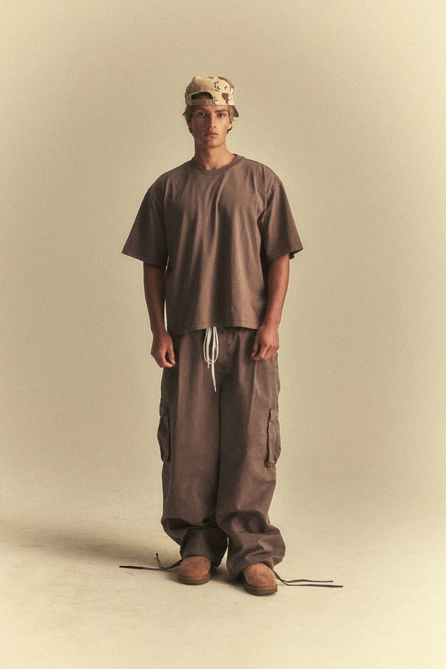 Person wearing a brown outfit with a cap on a beige background