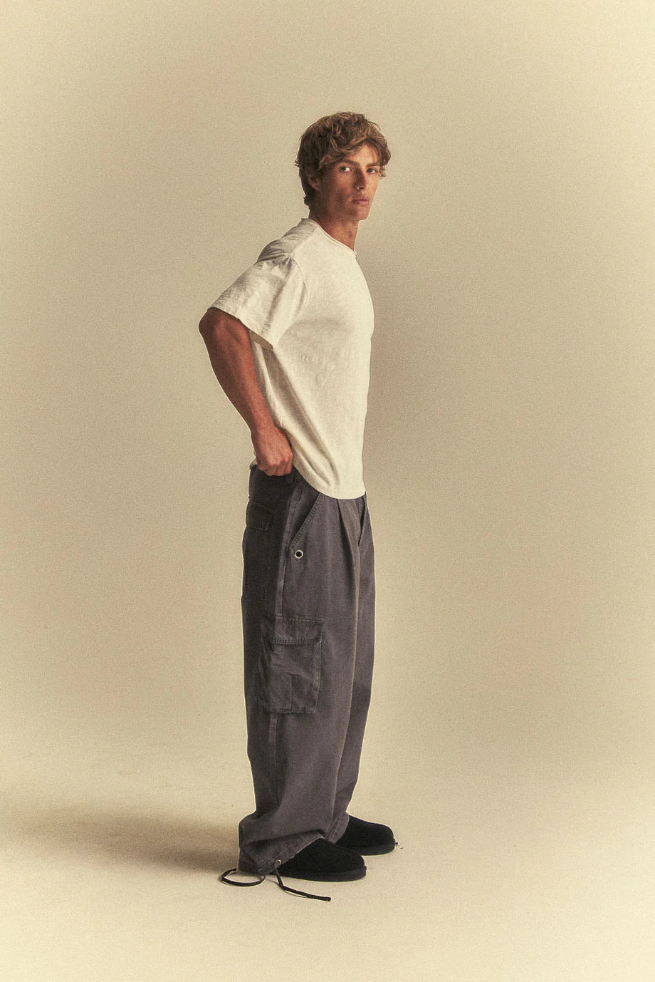 Man wearing a white t-shirt and grey cargo pants on a beige background