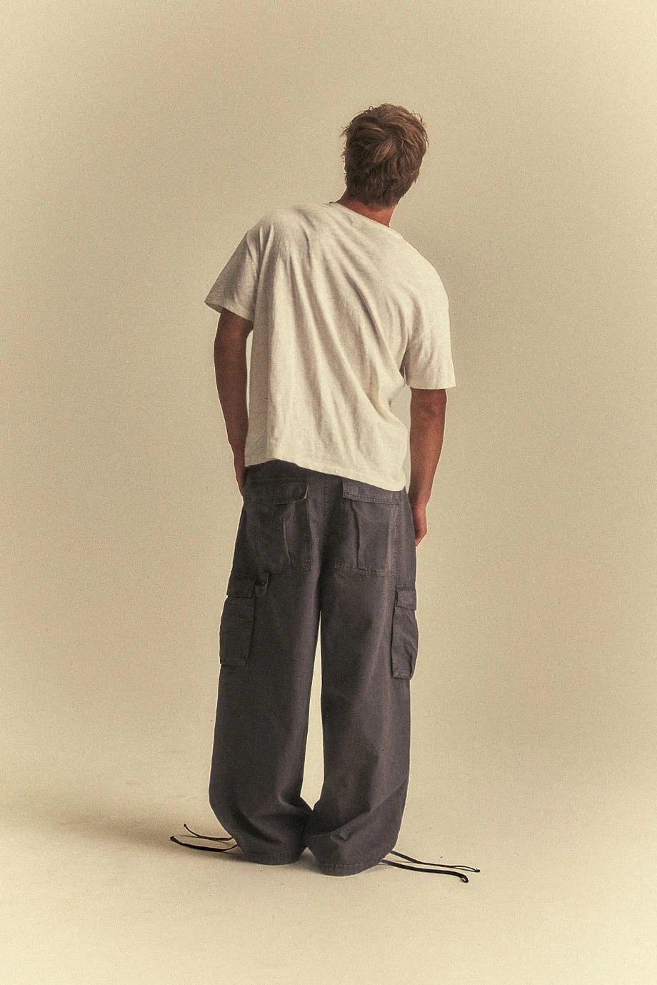 Person wearing a white t-shirt and dark cargo pants on a beige background