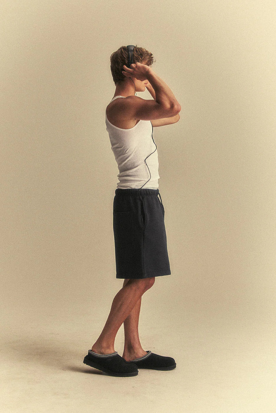 Person wearing a white tank top and black shorts on a beige background