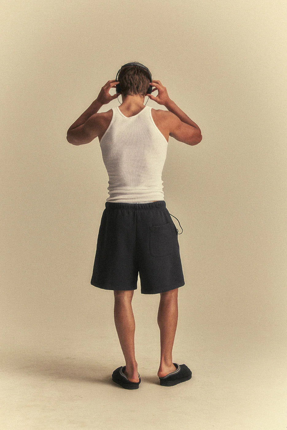 Person wearing a white tank top and black shorts on a beige background
