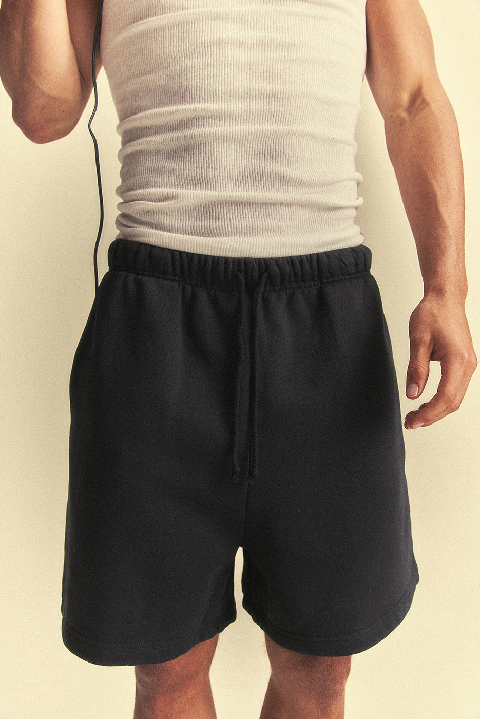 Person wearing black shorts and a beige tank top on a plain background