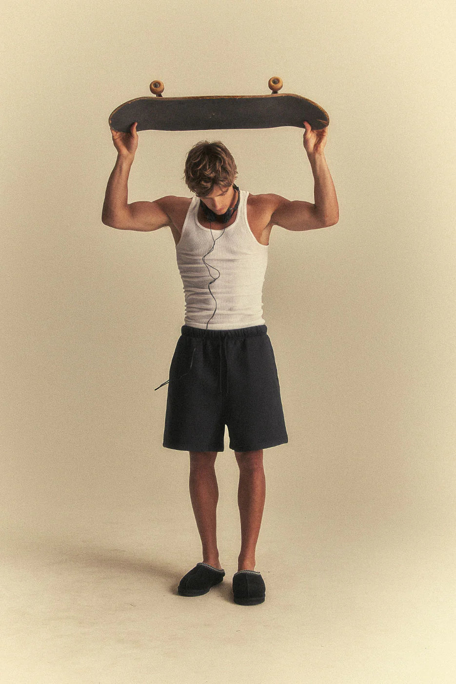 Person holding a skateboard above their head against a beige background