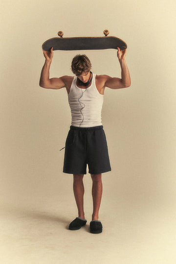 Person holding a skateboard above their head against a beige background