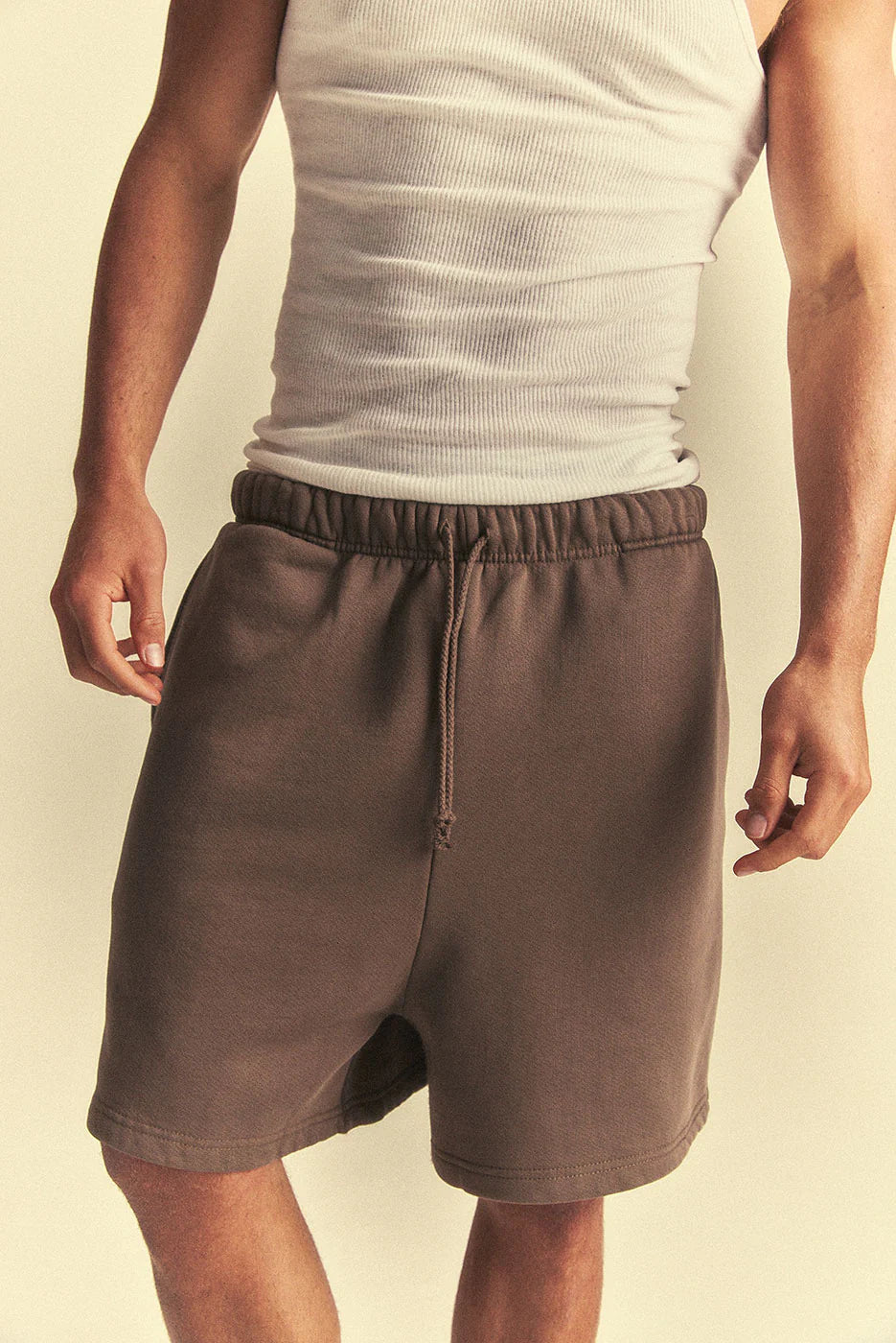Person wearing brown shorts and a light grey tank top on a beige background