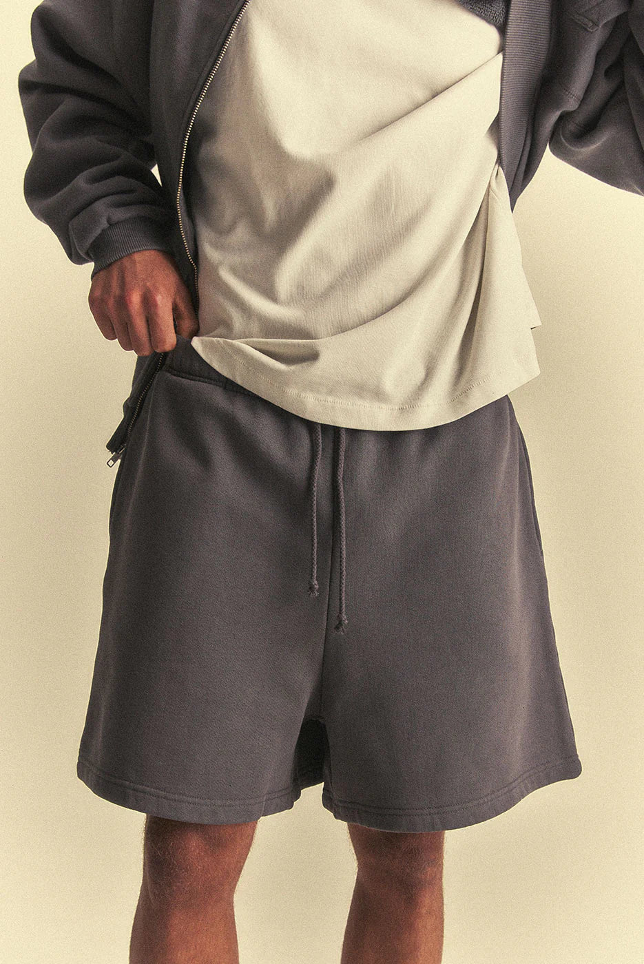 Person wearing dark grey shorts and a light-colored shirt on a beige background