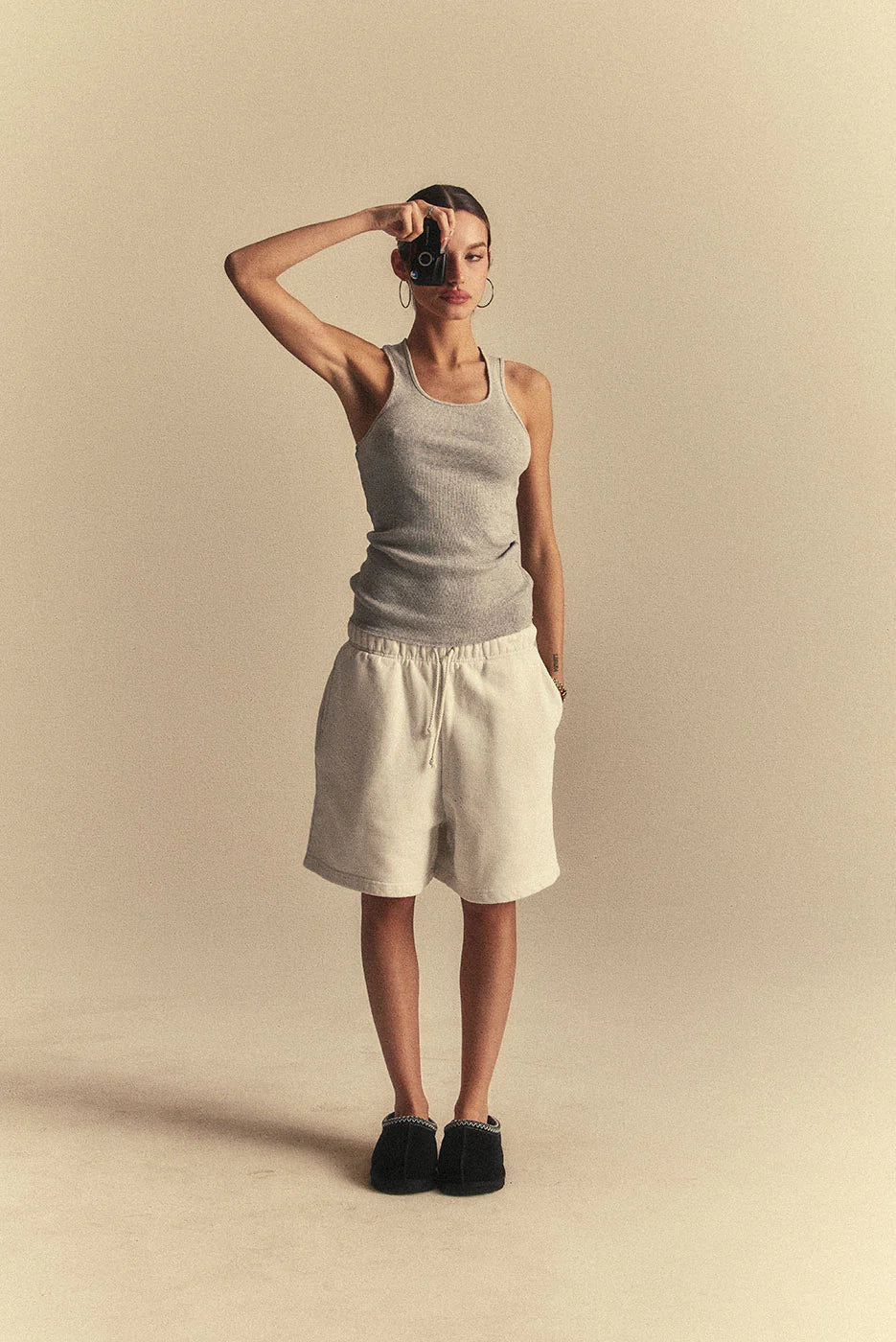 Person wearing a grey tank top and white shorts against a beige background