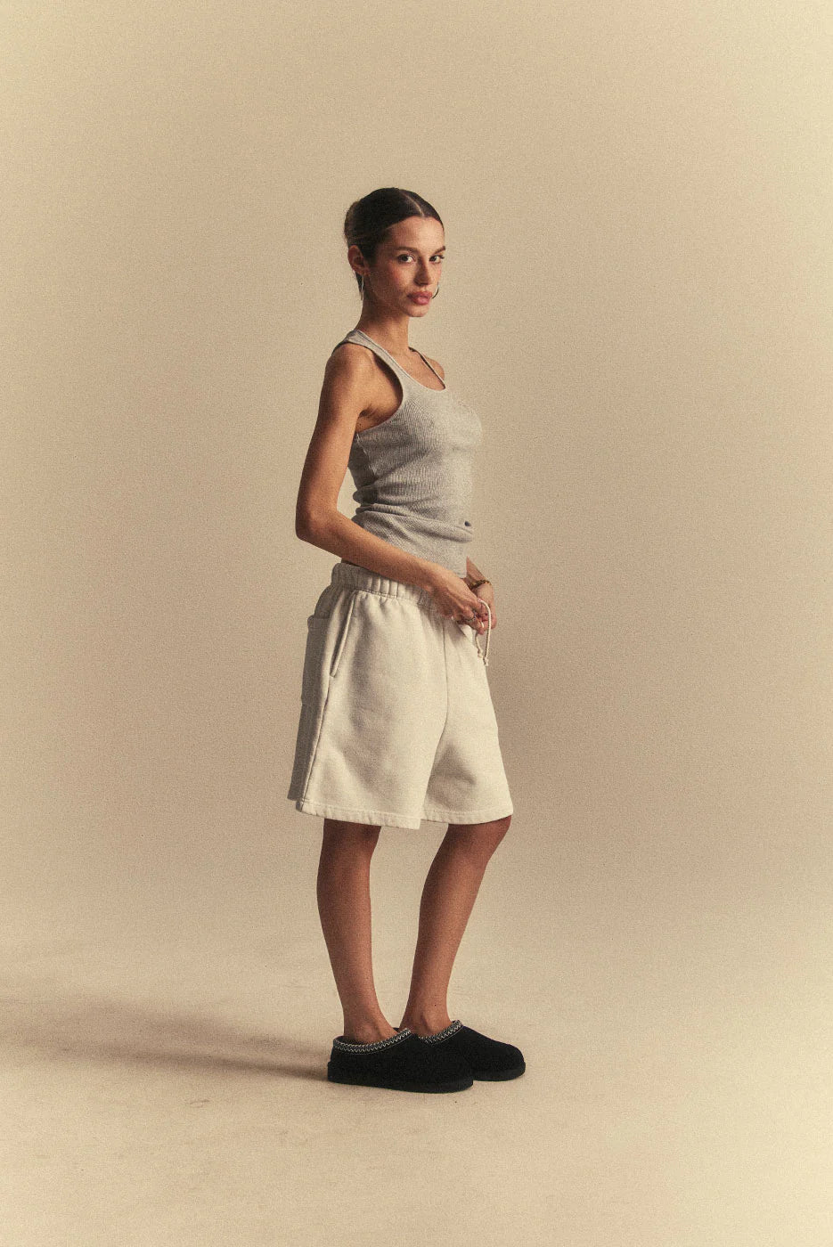 Woman wearing a light grey tank top and beige shorts against a beige background