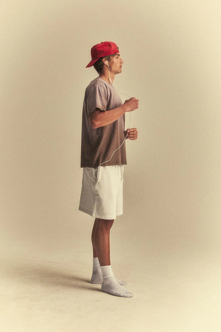 Man wearing a red cap, brown t-shirt, white shorts, and grey socks on a beige background