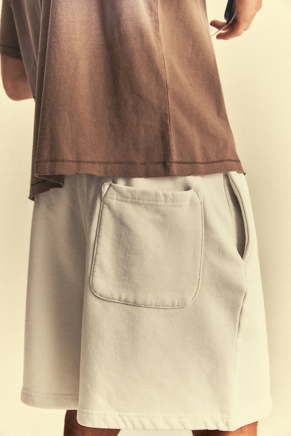 Person wearing a brown shirt and beige shorts on a plain background